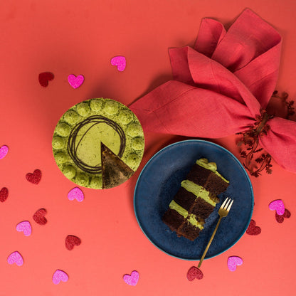 Green and brown cake on a blue plate with a red napkin and heart-shaped decorations on a red background