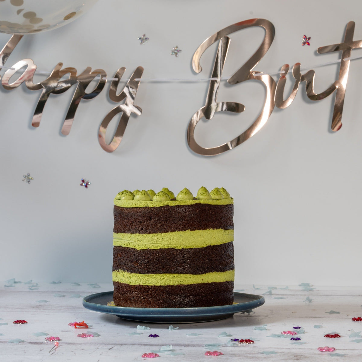 Two-layered cake with green and brown stripes on a decorative tablecloth with 'Happy Birthday' banner.