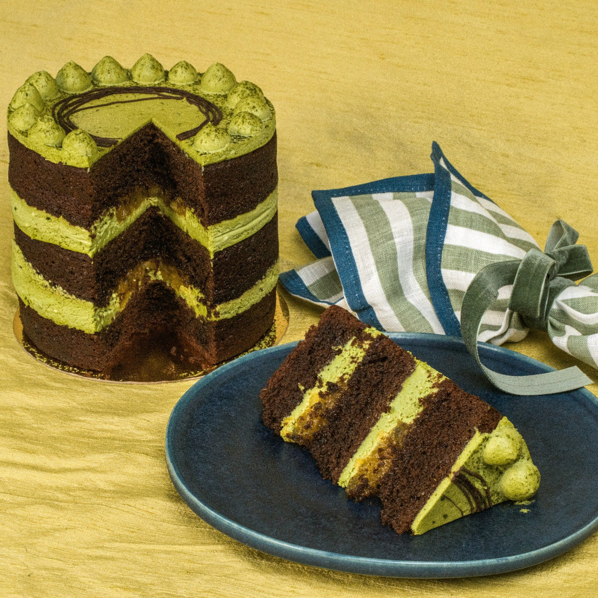 Striped chocolate and green cake with a slice on a blue plate, set against a wooden background.