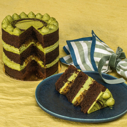 Striped chocolate and green cake with a slice on a blue plate, set against a wooden background.